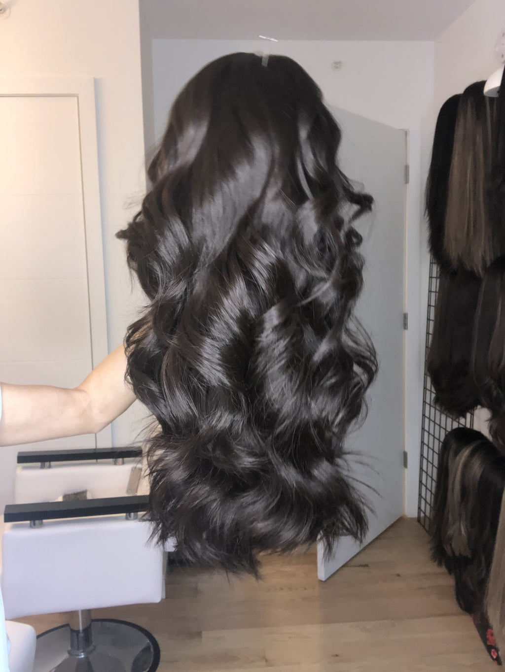Long dark brown human hair wig with loose waves, held up to show volume and texture in a salon setting.